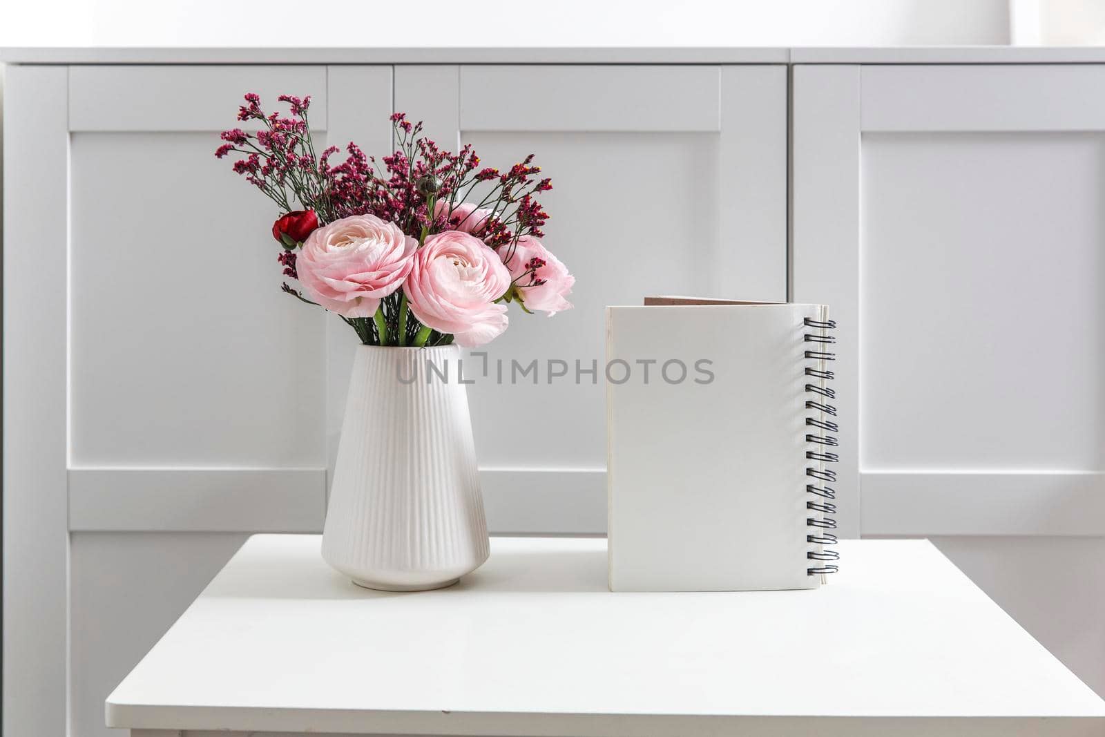 Bouquet of pink Persian buttercups on a white table in front of a chest of drawers. Scandinavian style. Place for text