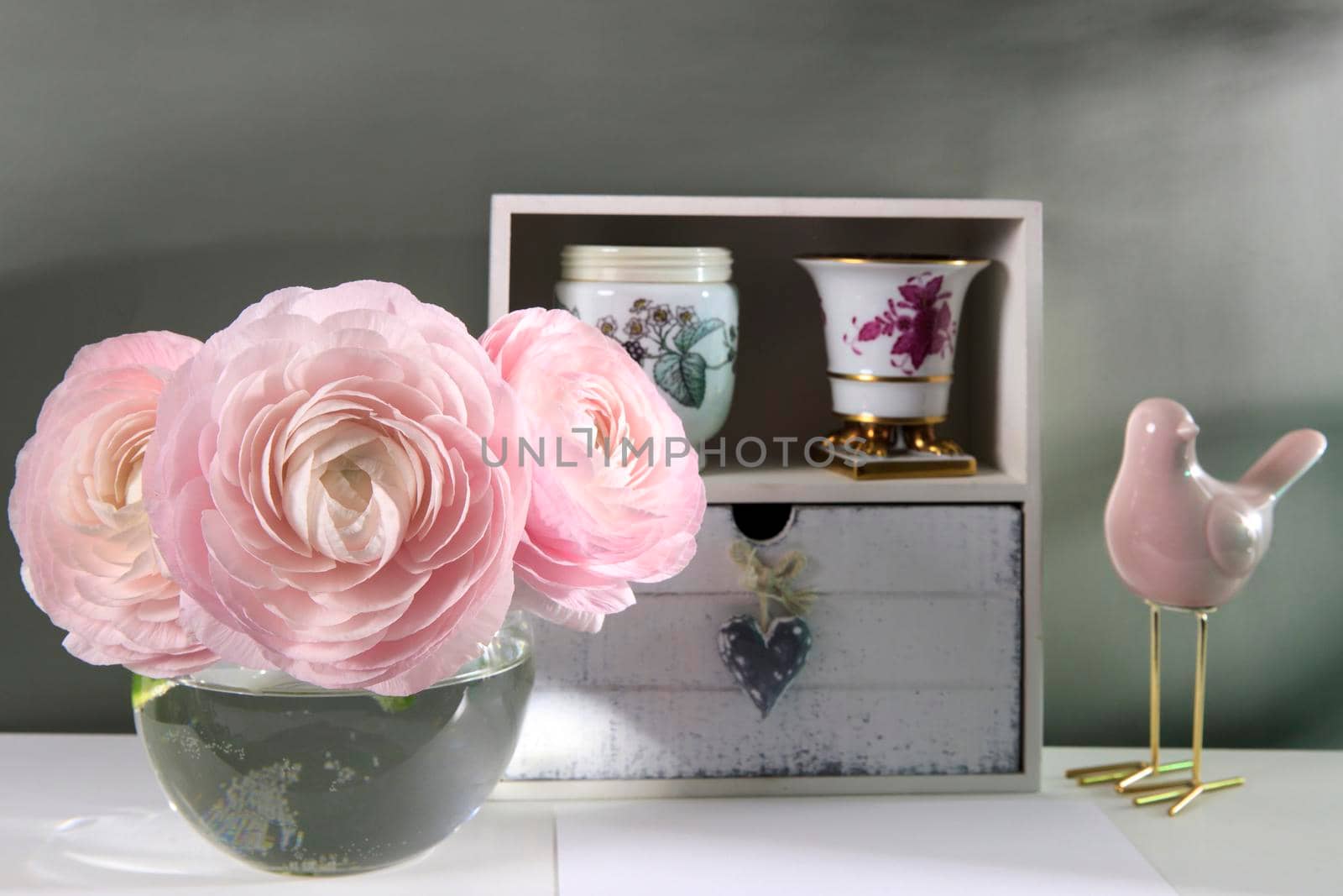 Three pale pink ranunculus in a transparent round vase on the white windowsill. Copy space. Place for text