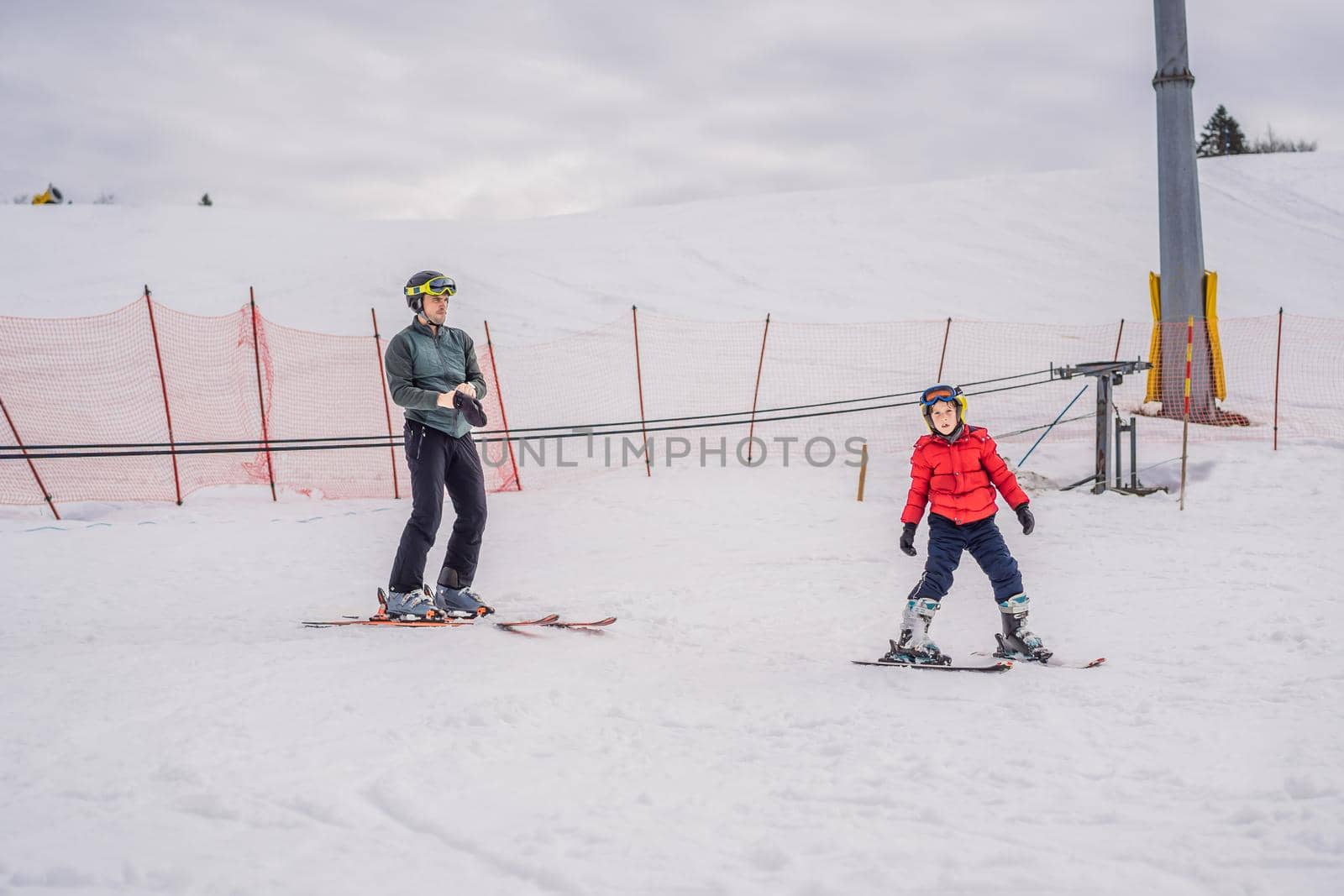 Boy learning to ski, training and listening to his ski instructor on the slope in winter.