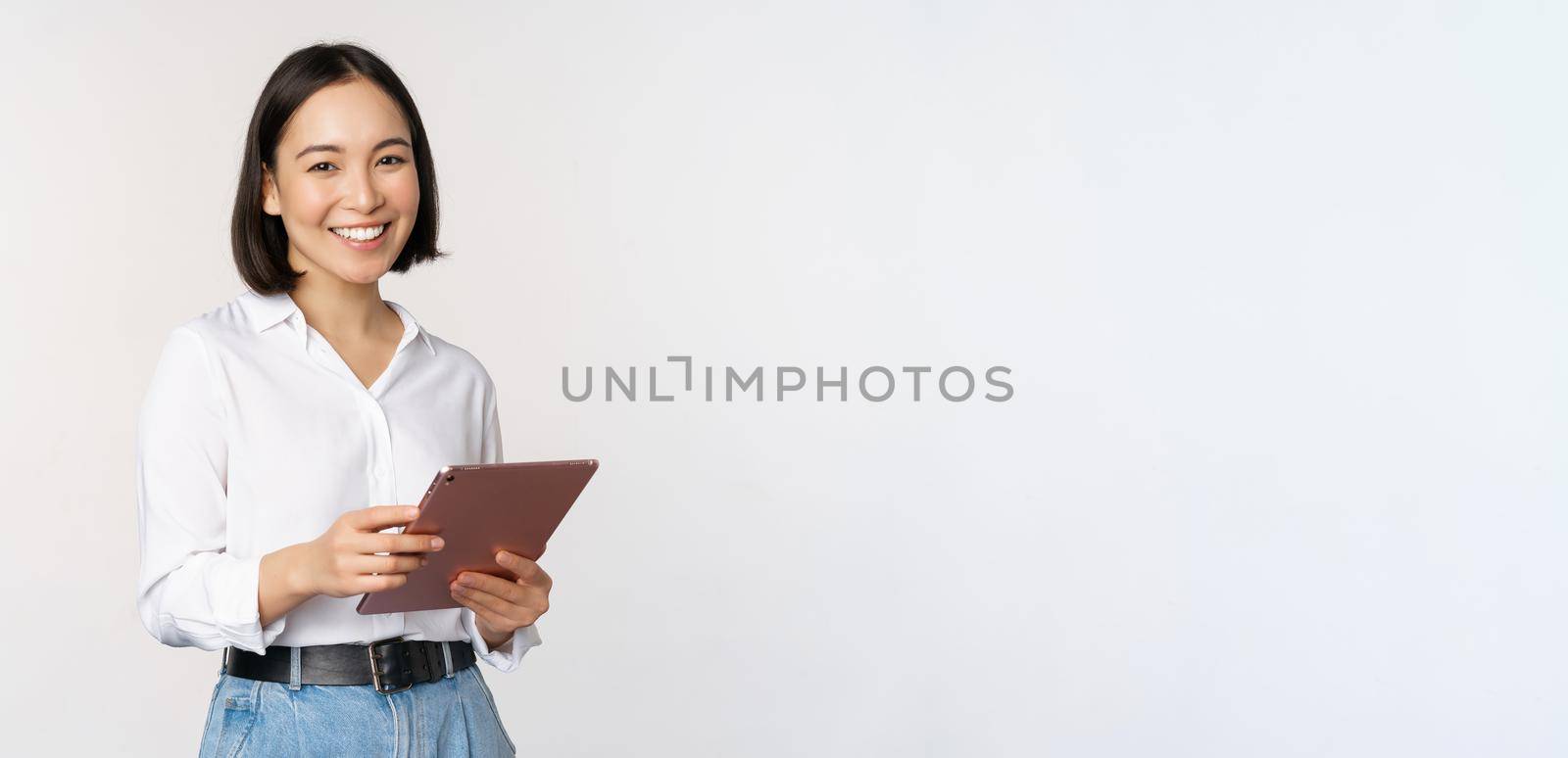Image of young ceo manager, korean working woman holding tablet and smiling, standing over white background.
