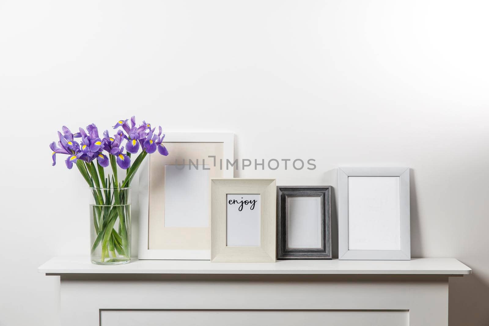 Bouquets of irises in a vase, photo frames on a chest of drawers by elenarostunova