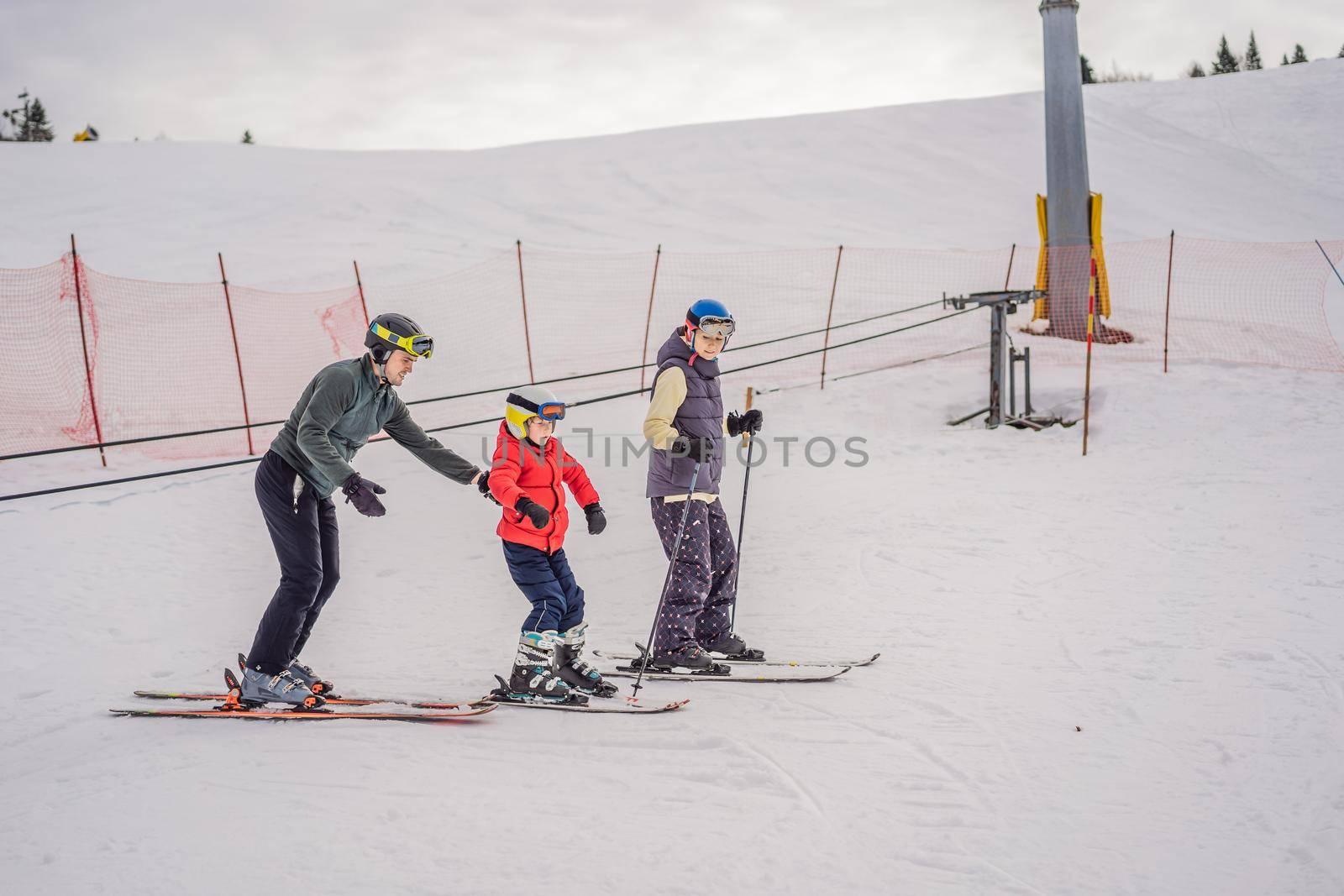 Mom and son are learning to ski with an instructor.Active toddler kid with safety helmet, goggles and poles. Ski race for young children. Winter sport for family. Kids ski lesson in alpine school. Little skier racing in snow.