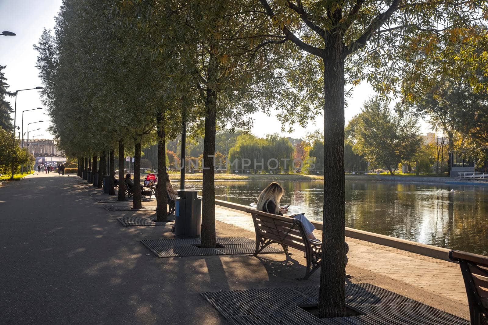 Moscow, Russia - 08 October 2021, Gorky Central Park of Culture and Leisure. A blonde girl sits on a bench near the pond, looks at the phone