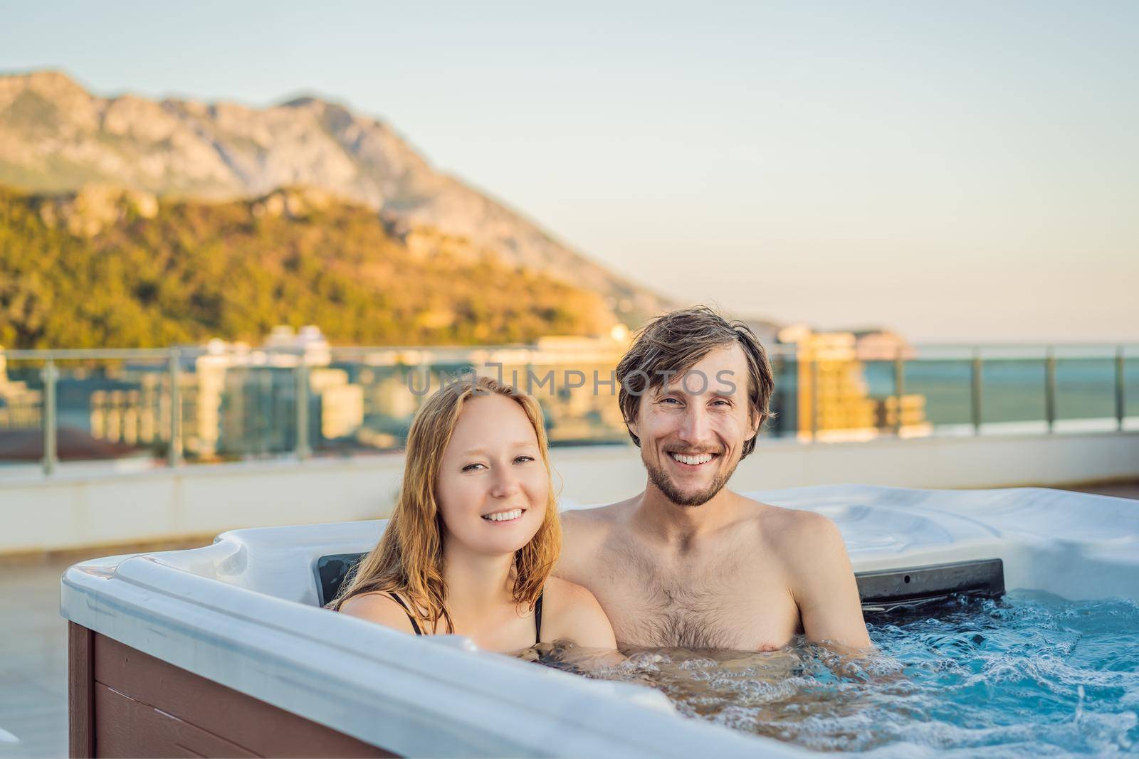 Portrait of young carefree happy smiling couple relaxing at hot tub during enjoying happy traveling moment vacation life against the background of green big mountains by galitskaya