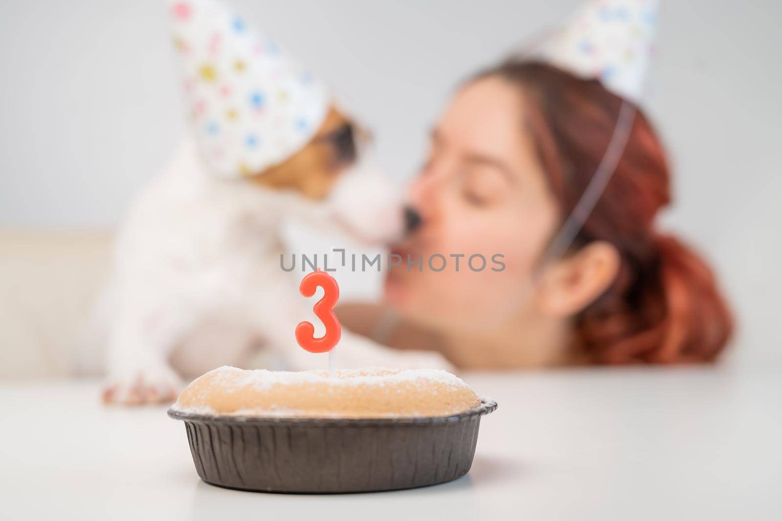 Caucasian woman congratulates her dog on the 3rd birthday. Jack russell terrier blows out the candle on the cake. by mrwed54