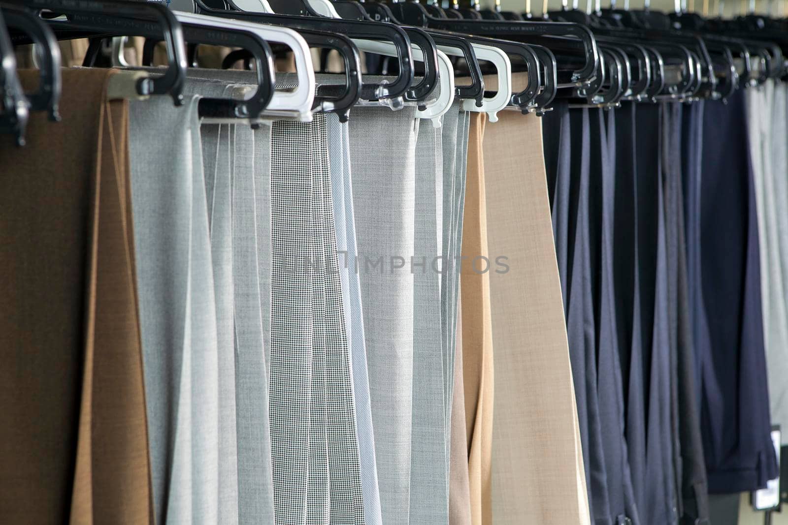 Men's gray and beige wool trousers hang on rails for sale in a store. Business style by elenarostunova