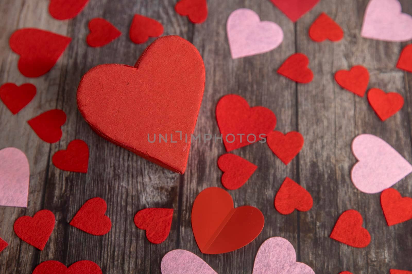 The red and pink paper and felt hearts of different shape and size are on a wooden brown table. The day of Valentine. Copy space by elenarostunova