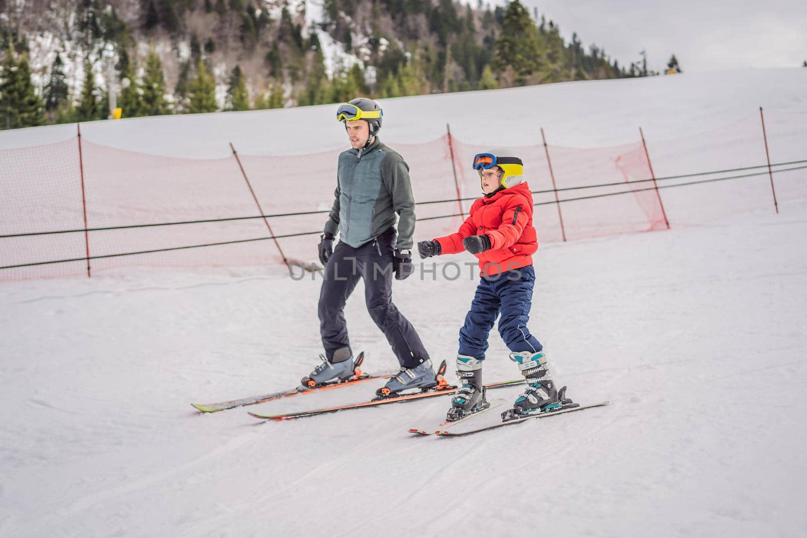 Boy learning to ski, training and listening to his ski instructor on the slope in winter.
