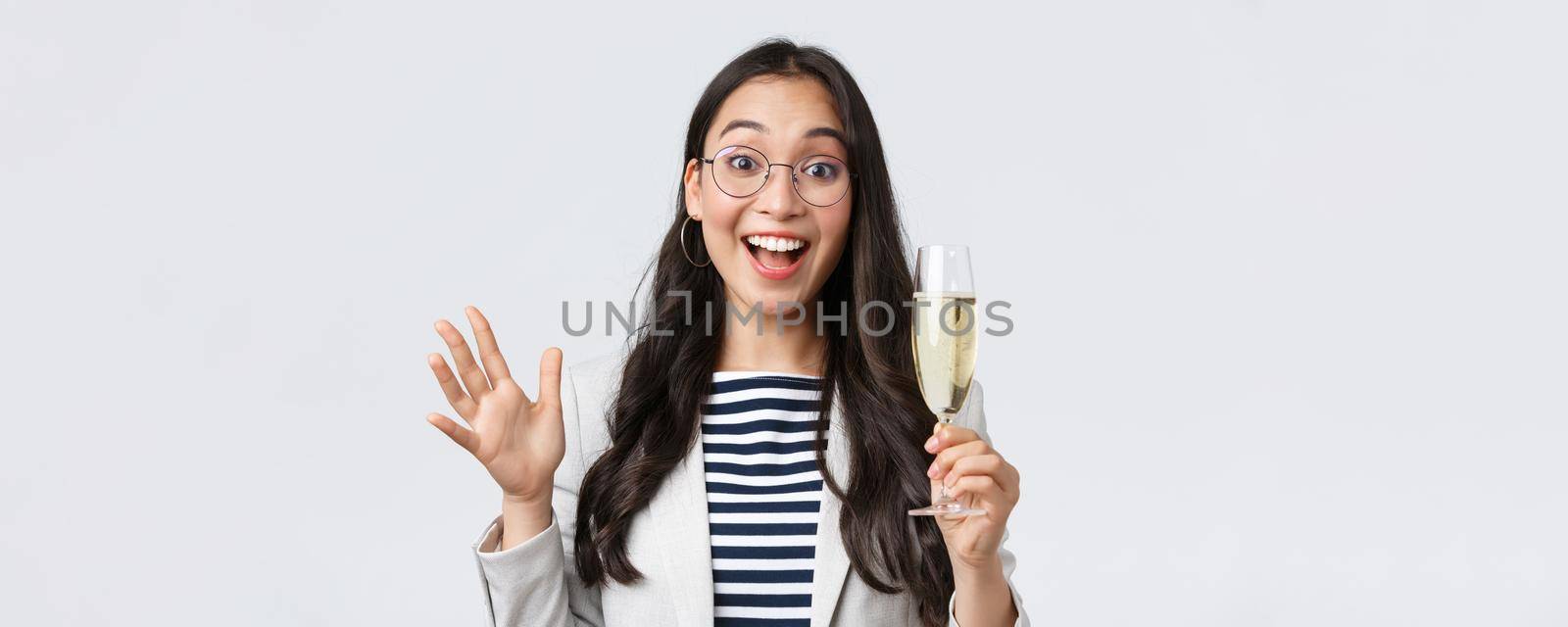 Business, finance and employment, female successful entrepreneurs concept. Friendly cheerful asian office worker enjoying party with colleagues, saying hi, drinking champagne and waving hand.