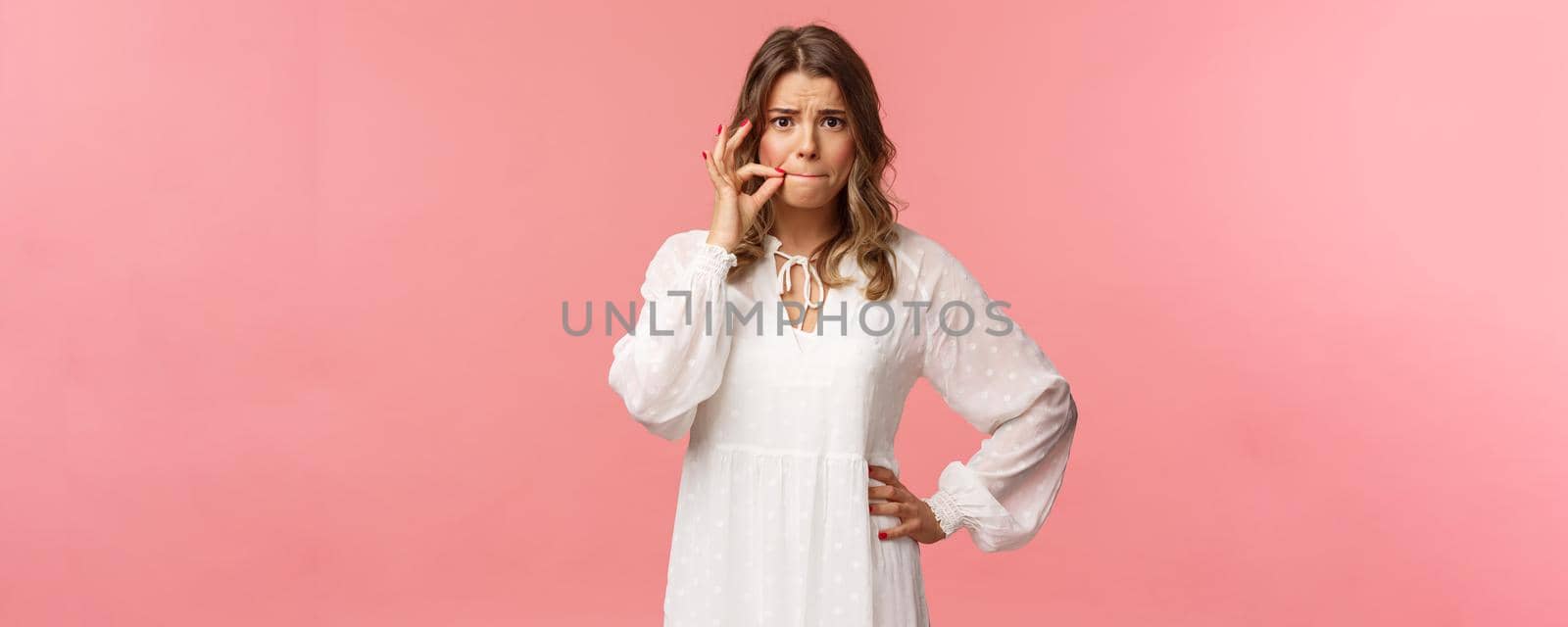 Worried cute blond girl give promise not tell anyone, make zip lips gesture and frowning concerned, heard someone secret, keep silent about situation, standing embarrassed pink background.
