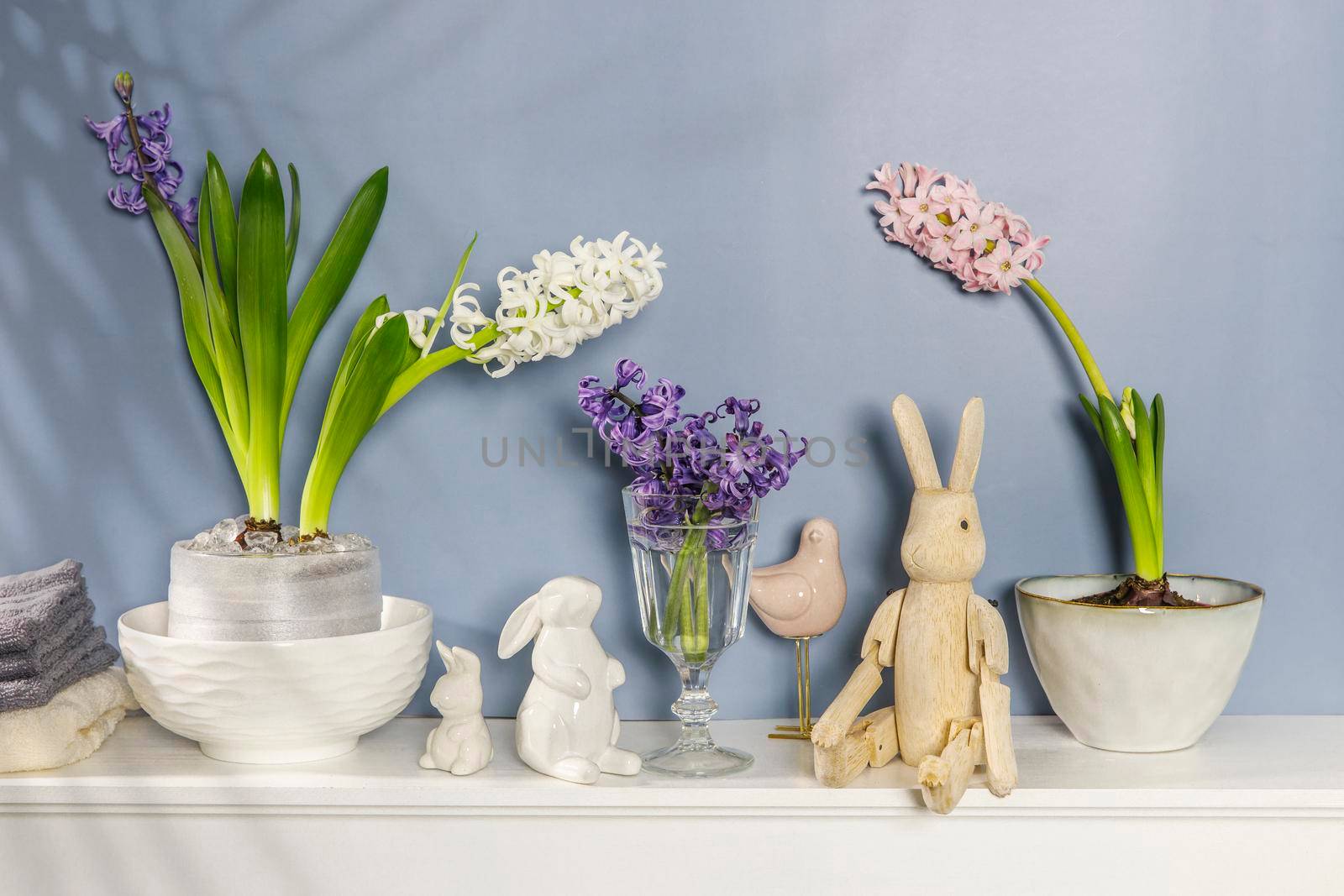 White hyacinth in a large porcelain bowl, figurines of hares and a bird, are on the fireplace against the dark blue wall. Layout. Spring concept