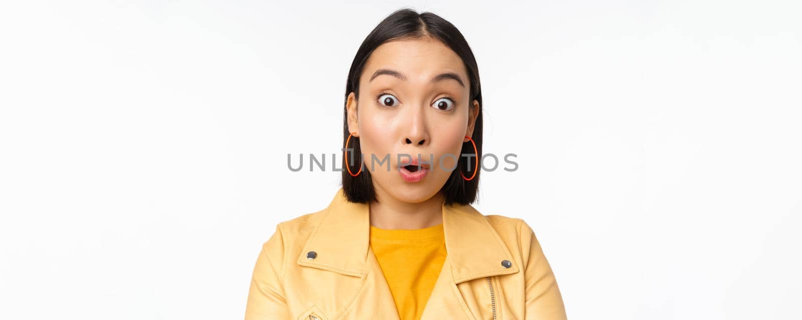Close up of impressed asian girl, say wow, looking amazed at camera, standing in casual clothes over white background. Copy space