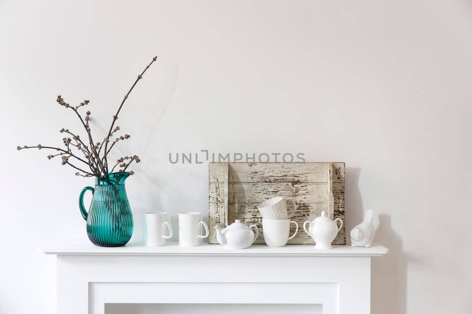 American maple branches in a green glass jar, porcelain cups, figurines, teapot on a white chest of drawers. Scandinavian style