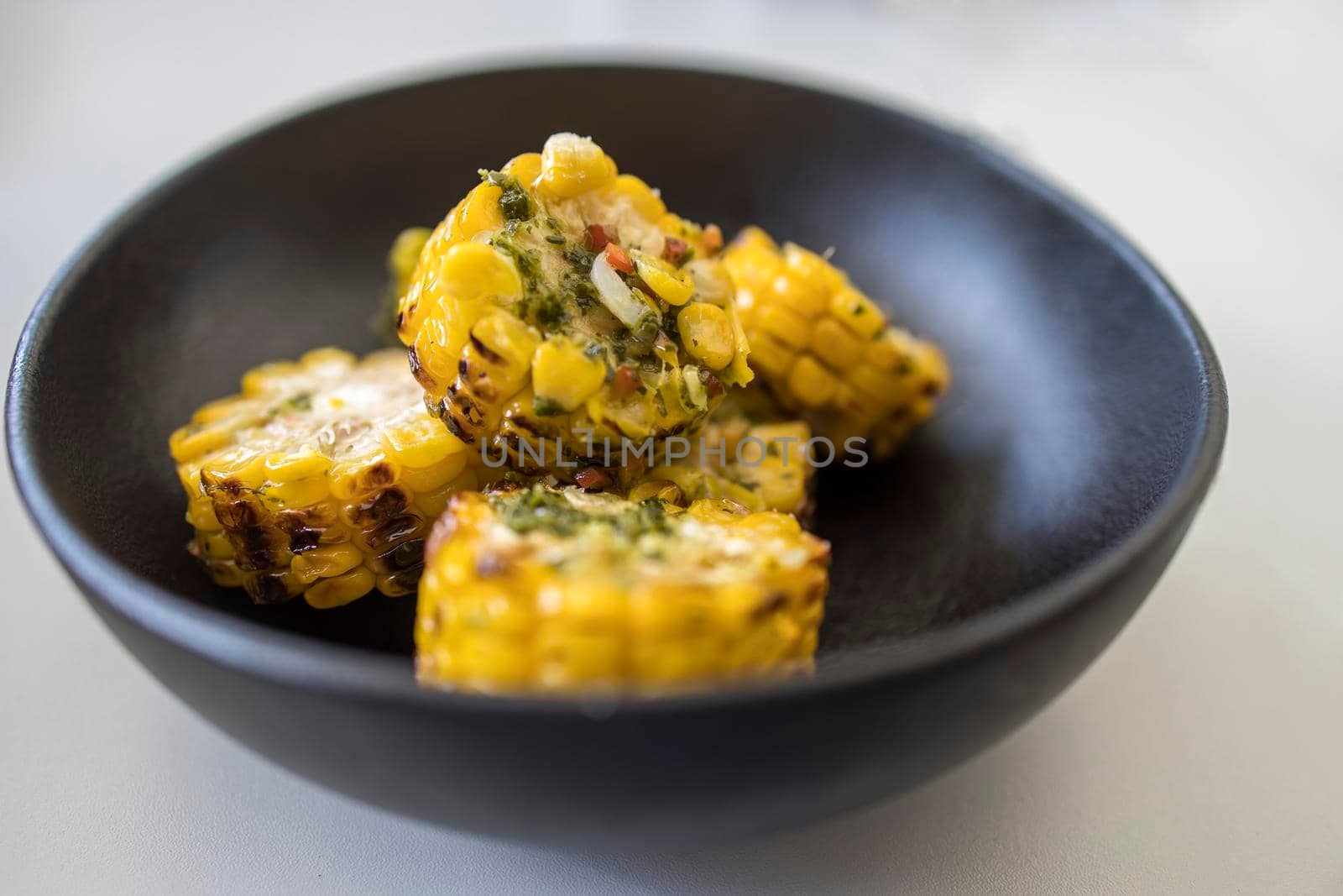 Chopped, grilled spiced corn in a black ceramic plate by elenarostunova