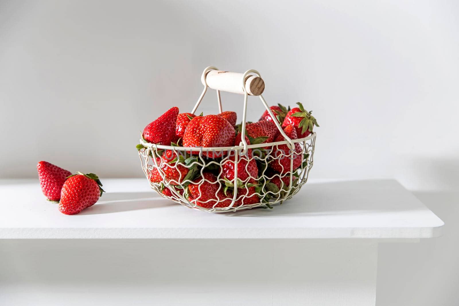 White metal basket with wooden handle with fresh strawberries on beige table by elenarostunova