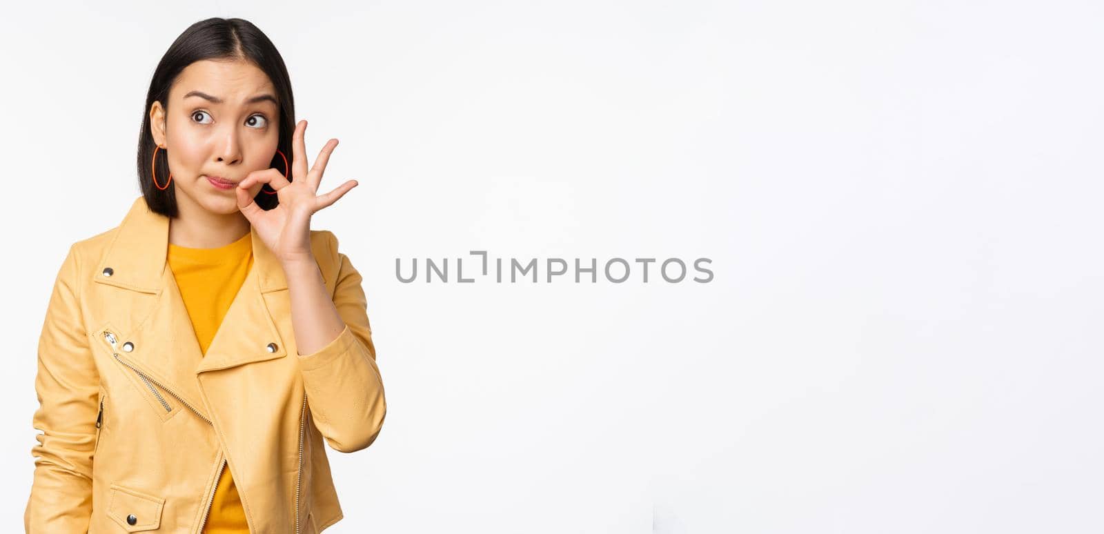 Image of young asian woman seal lips, silence gesture, zipping her mouth with promise, standing over white background.