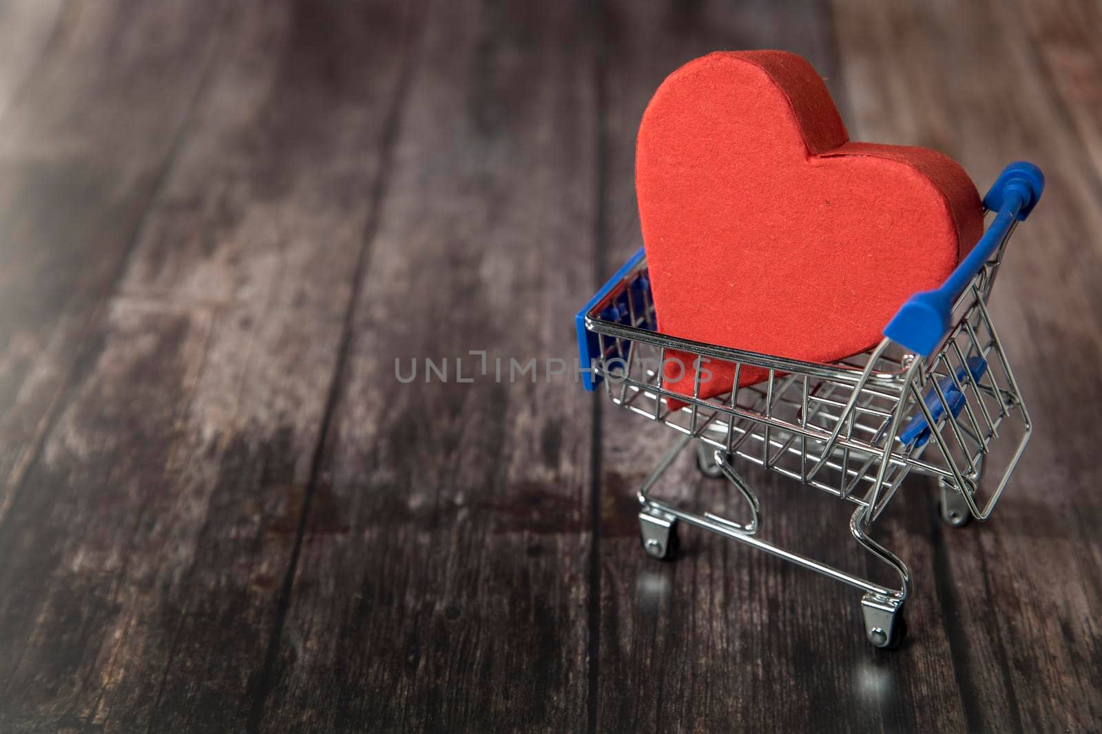 A supermarket trolley with the big paper heart, home delivery of love are on the brown wooden background. Copy space by elenarostunova