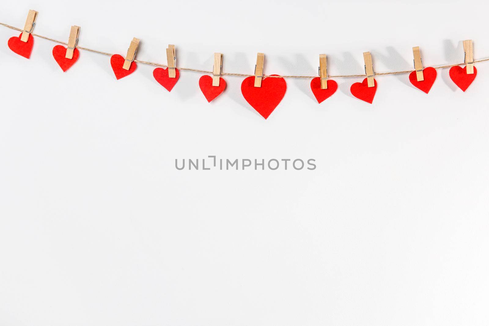 A handmade garland of the hearts is on a white wall. Place for text. Copy space by elenarostunova