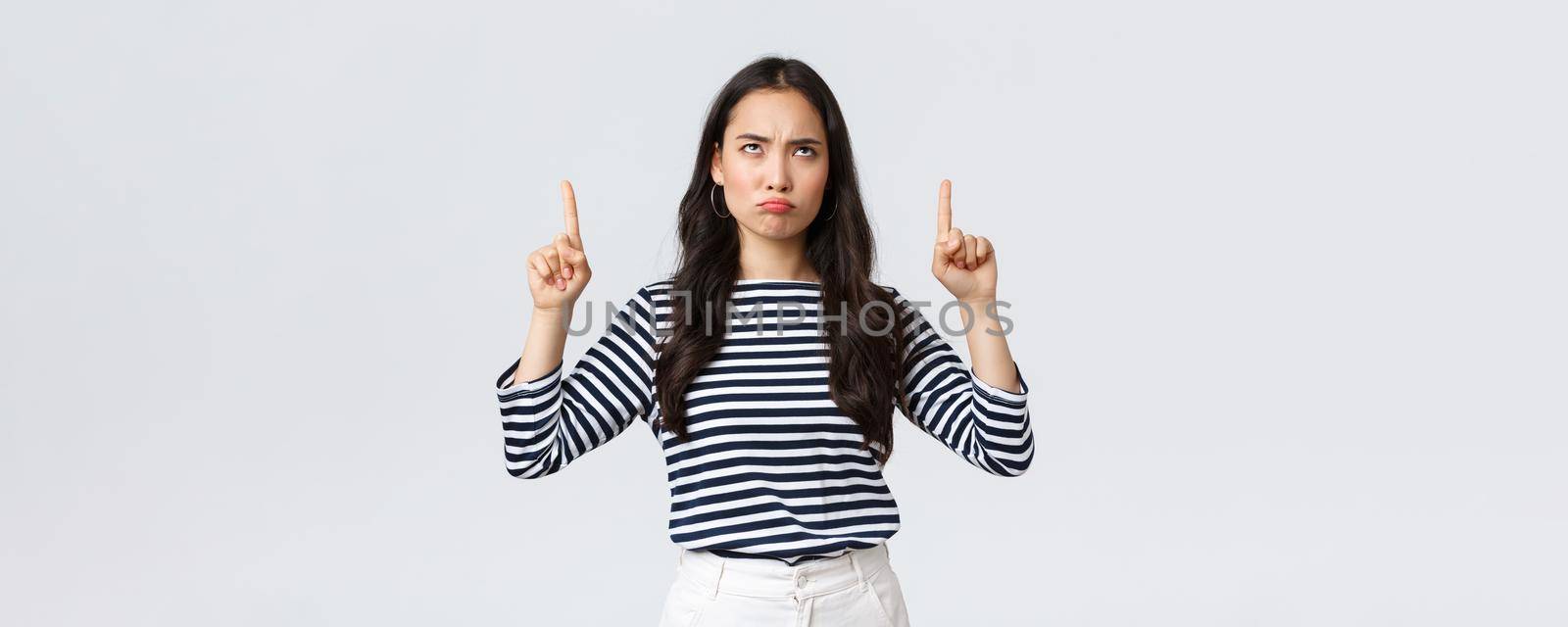 Lifestyle, beauty and fashion, people emotions concept. Skeptical and disappointed moody asian girlfriend complaining, pouting unsatisfied and pointing fingers up.