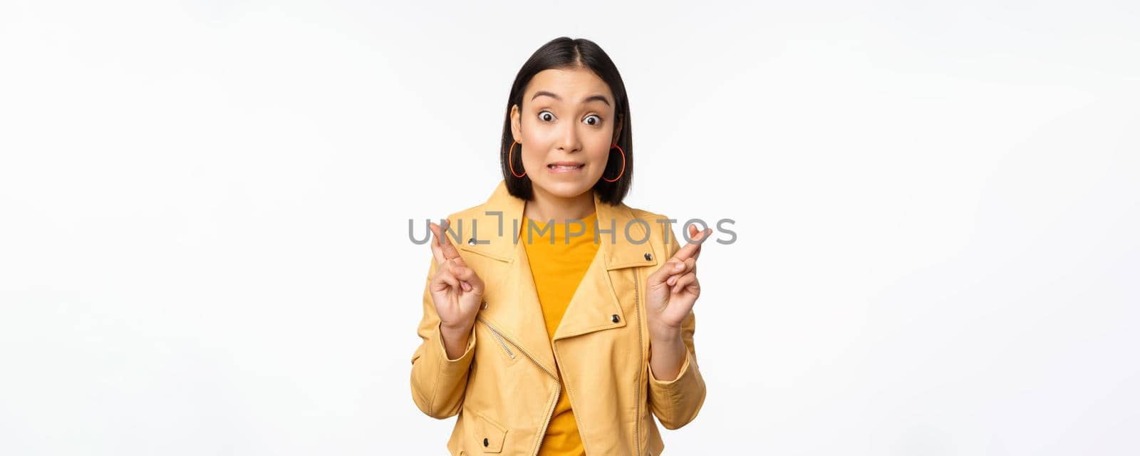 Portrait of excited asian woman looks hopeful, wishing, praying or begging, waiting for news, standing over white background, smiling enthusiastic.
