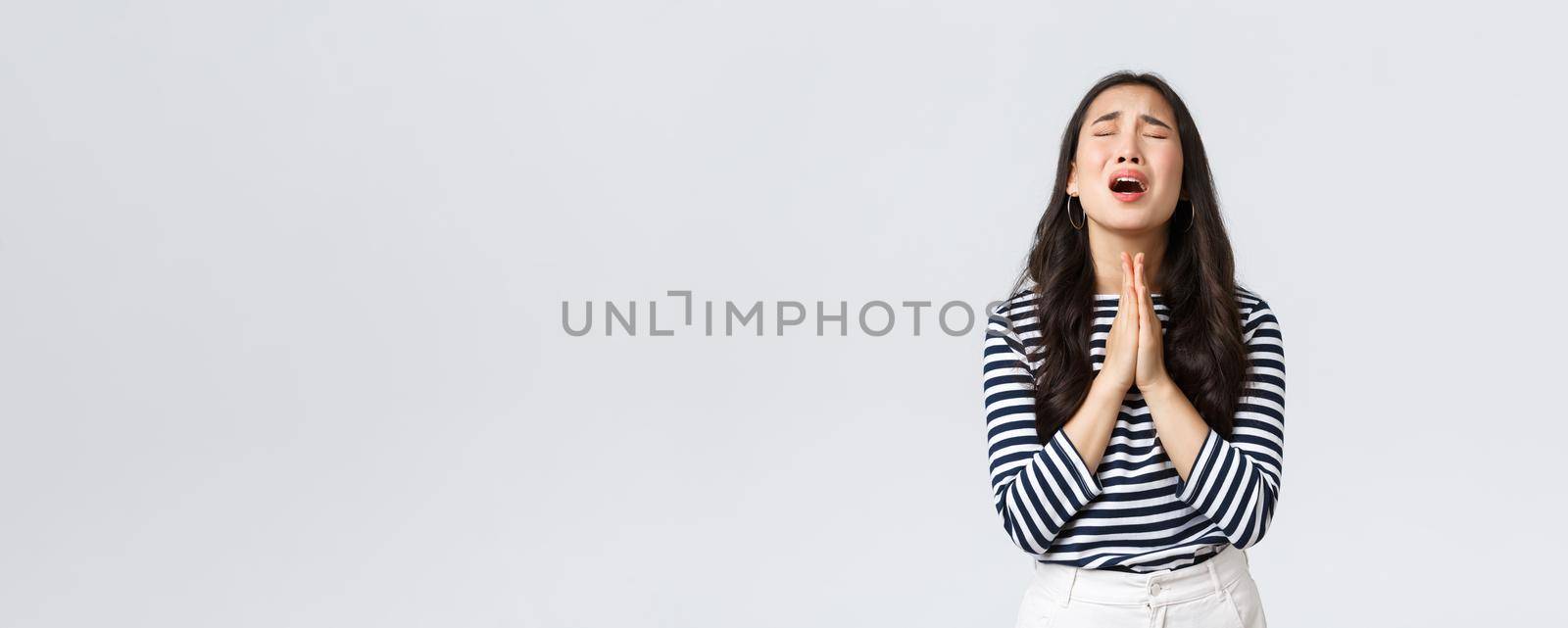 Lifestyle, people emotions and casual concept. Desperate hopeful asian girl making wish, close eyes and hold hands in pray, pleading god to have something, making wishful face, white background.
