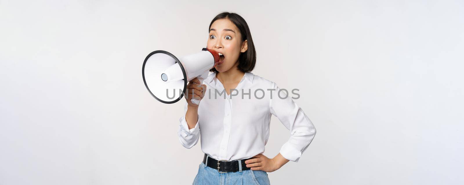 Image of young woman, korean activist, recruiter screaming in megaphone, searching, shouting at loudspeaker, standing over white background by Benzoix