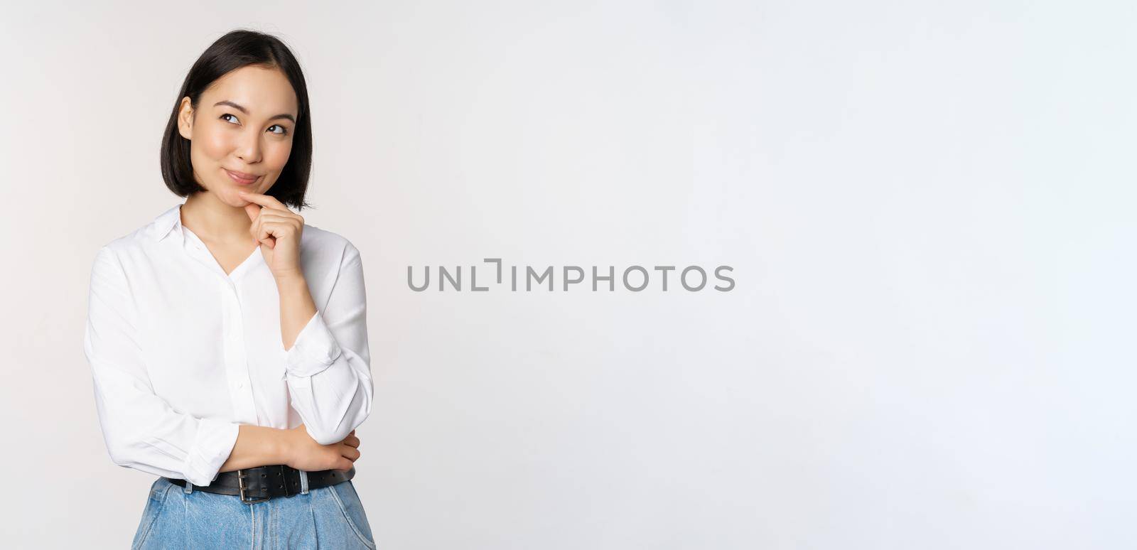 Image of thoughtful smiling woman has an idea, scheming, planning, looking aside and thinking, standing in office white blouse against studio background by Benzoix