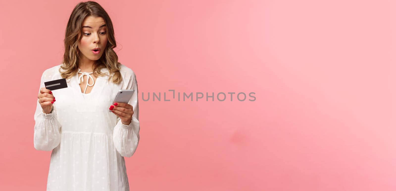 Excited and intrigued young blond girl in white dress, hurry up and make order on online shopping site before discount ends, enter credit card digit numbers to mobile phone, pink background by Benzoix