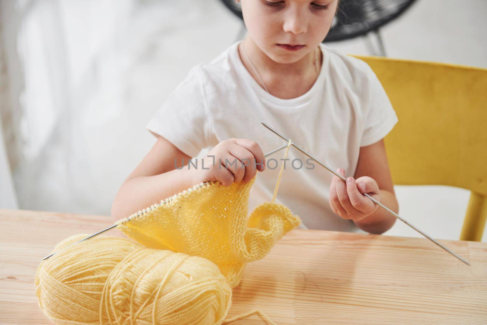 Doing homework. Kid is knitting. Cute little girl sitting near the wooden table is learning some new stuff.