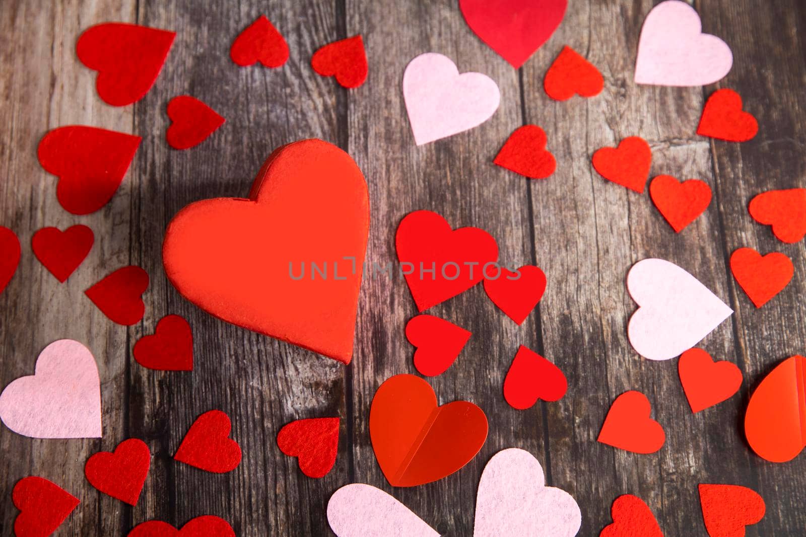 The red and pink paper and felt hearts of different shape and size are on a wooden brown table. The day of Valentine. Copy space