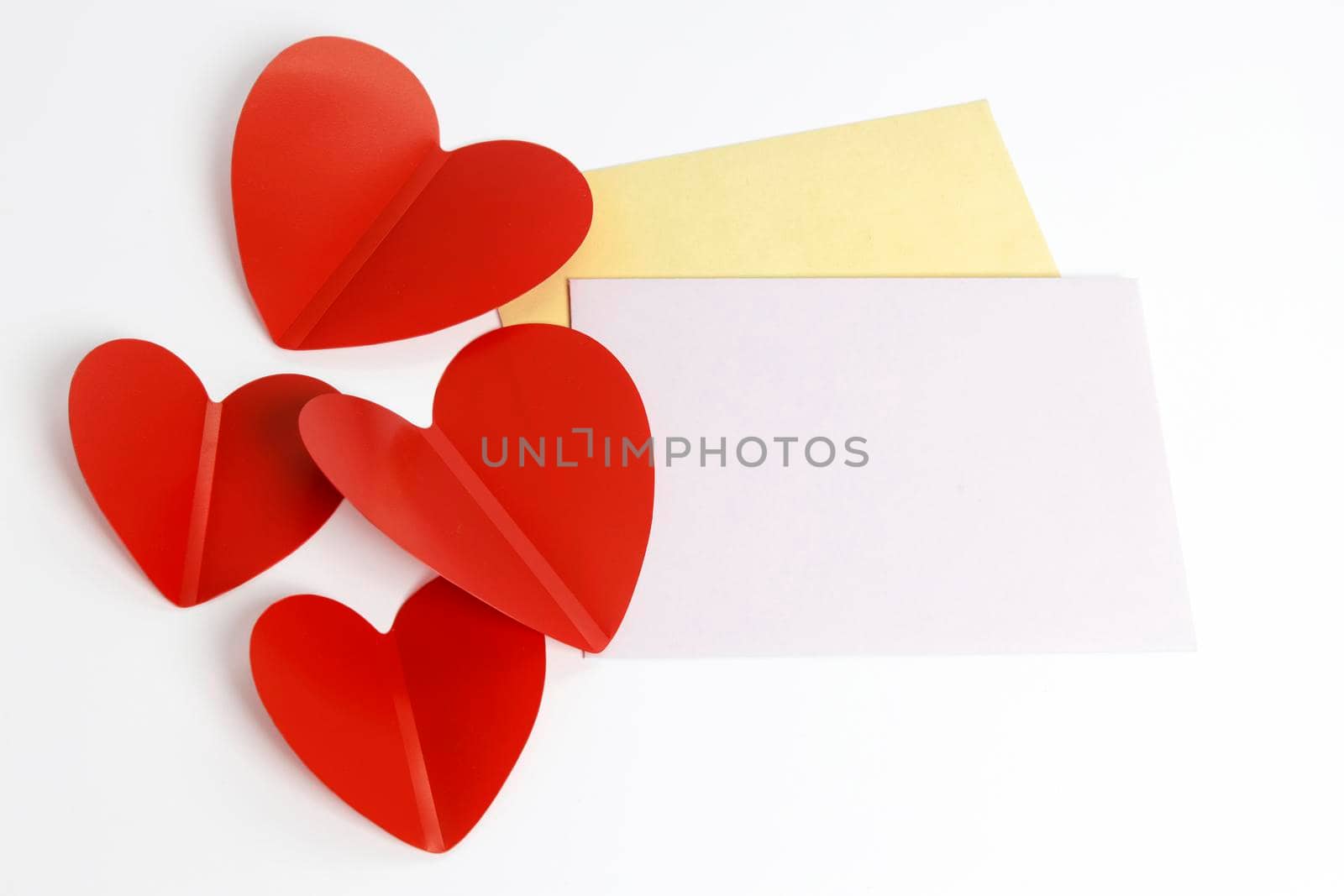 Greeting card for Valentine's Day. Envelopes on a white background and red plastic hearts. Copy space.