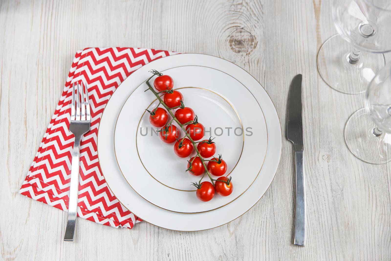 Serving plate, spoon, fork, knife and red napkin are on the wooden table. The concept of weight loss and diet. Tomatoes on two large plates by elenarostunova