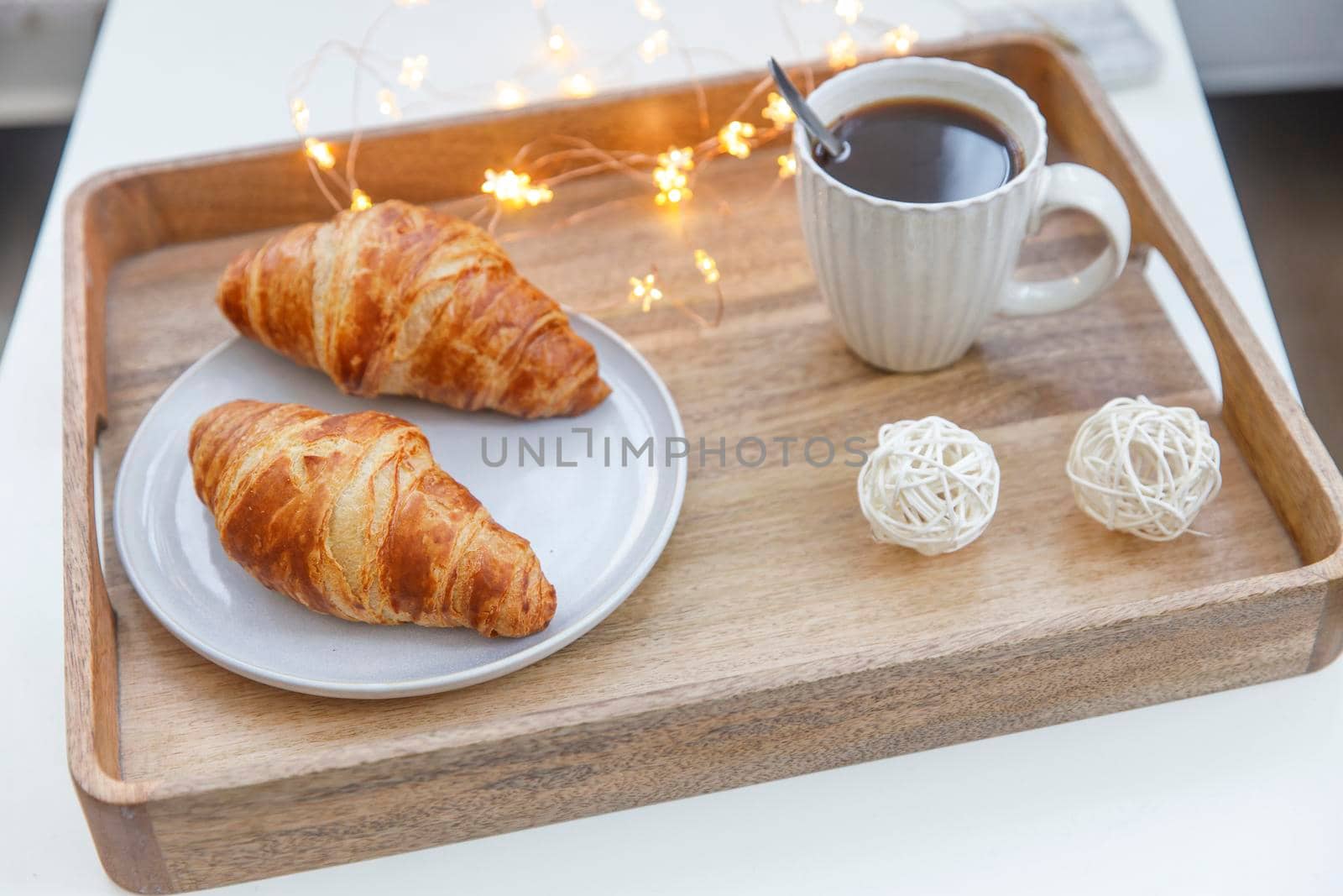 Freshly baked croissant on a gray round plate, white cup with coffee and garland on a tray on the table