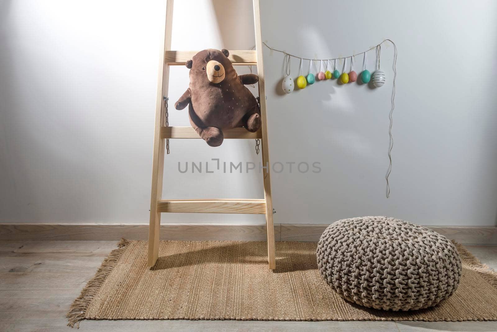 Fragment of the interior of the children's room, decorated for Easter. A ladder with a bear, a garland of fake colored eggs. Easter card by elenarostunova