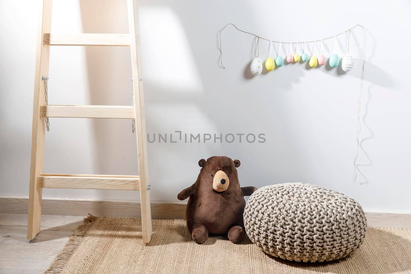 Fragment of the interior of the children's room, decorated for Easter. A ladder with a bear, a garland of fake colored eggs. Easter card