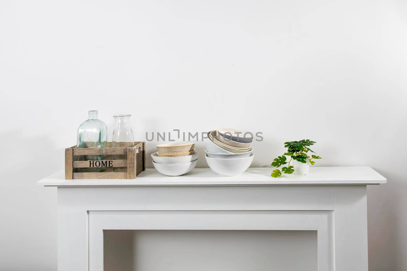 kitchen utensils, cups, bowls, bottles, storage items, artificial monstera in a ceramic pot are on a white dresser by elenarostunova