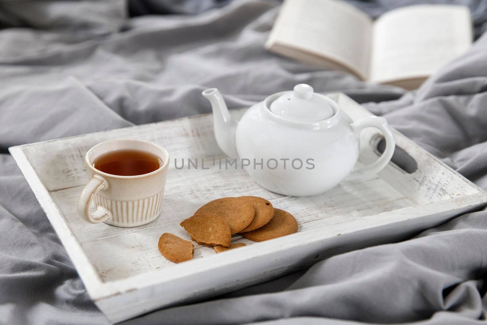 interior and home coziness concept. Top view. A cup of tea, a teapot with herbal tea, sugar bowl on a wooden tray on the bed. Porcelain cup