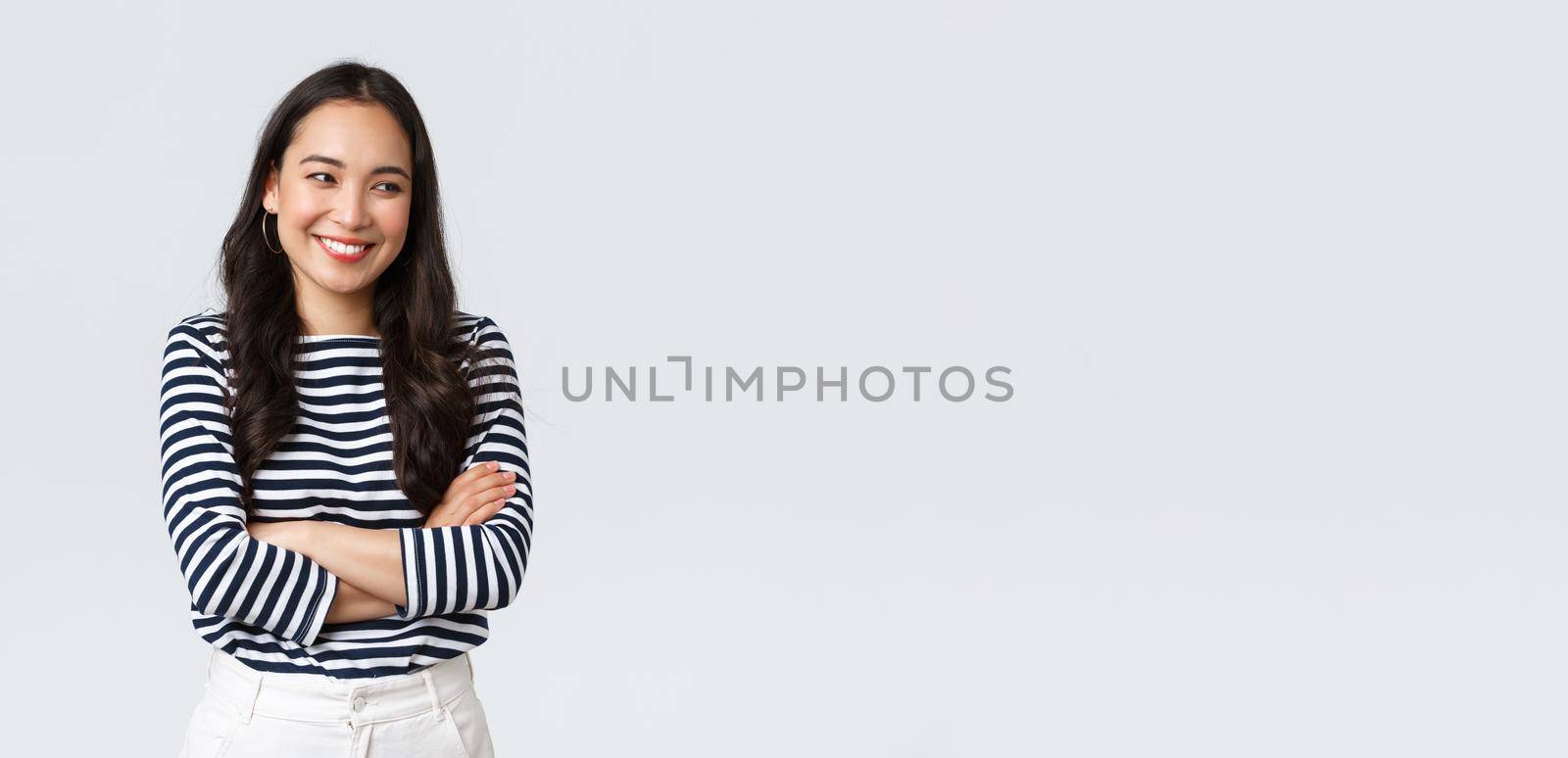 Lifestyle, beauty and fashion, people emotions concept. Cheerful cute and shy asian girl cross arms chest modest pose, looking away as laughing and smiling silly, stand white background.