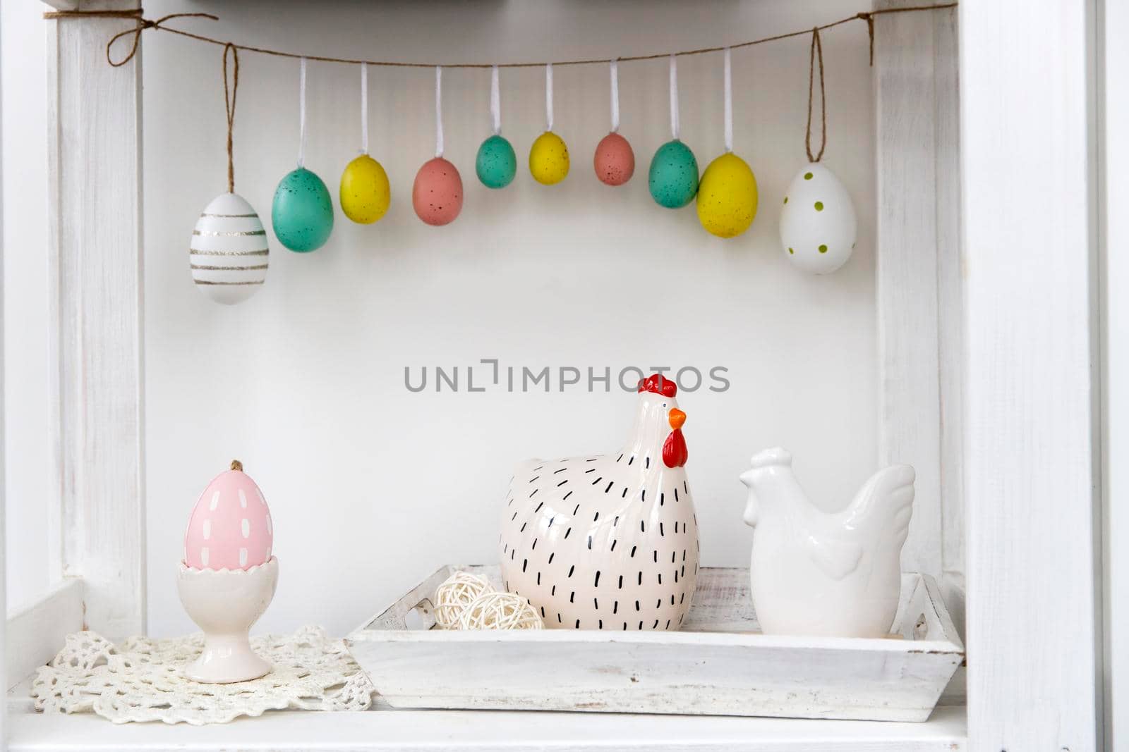 Fragment of the interior. Decorated children's room for Easter. A garland of plastic eggs on the wall. Ceramic hens on the tray on the table. Place for your text. Easter card.