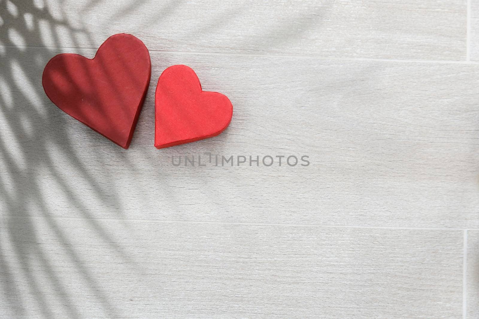 Two paper hearts and a shadow from a palm branch are on the tiled beige tiles. Space for text. Copy space. by elenarostunova