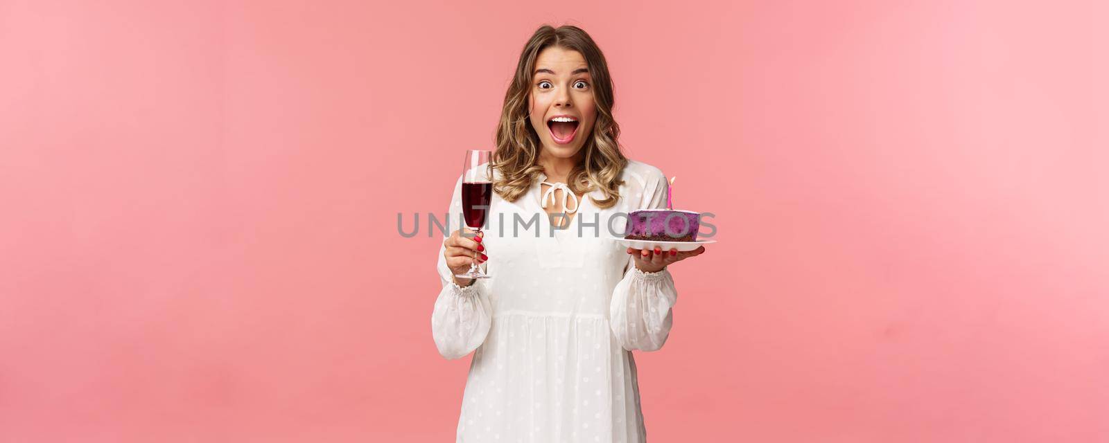 Holidays, spring and party concept. Portrait of fascinated and amused blond girl in white dress look astonished camera, celebrating birthday with b-day cake and glass of wine, pink background by Benzoix