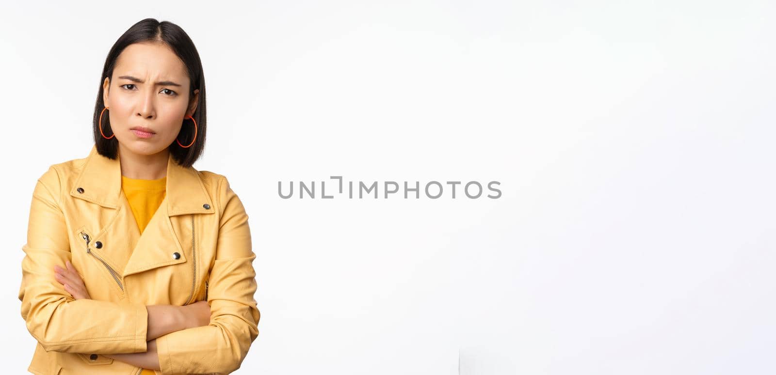 Image of asian girl looking angry and hurt, staring with upset, offended face expression, standing over white background. Copy space
