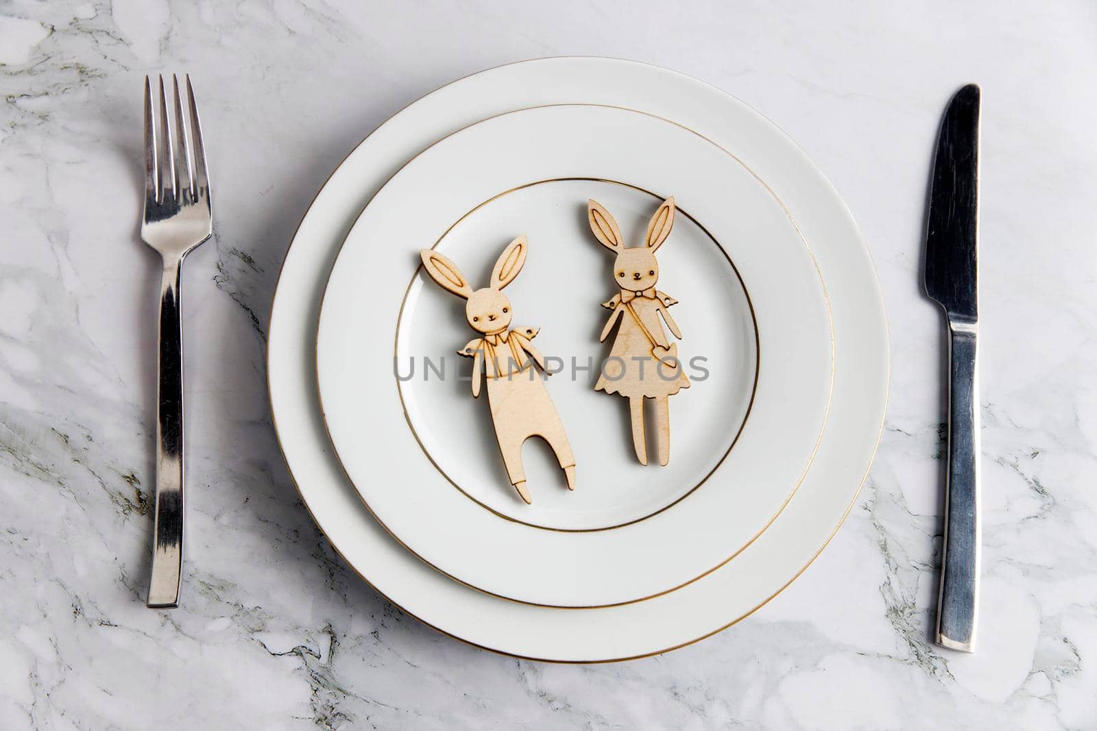 Serving spoon, fork, knife, and two carton bunny on the plate on the marble table. The concept of decoration for Easter.