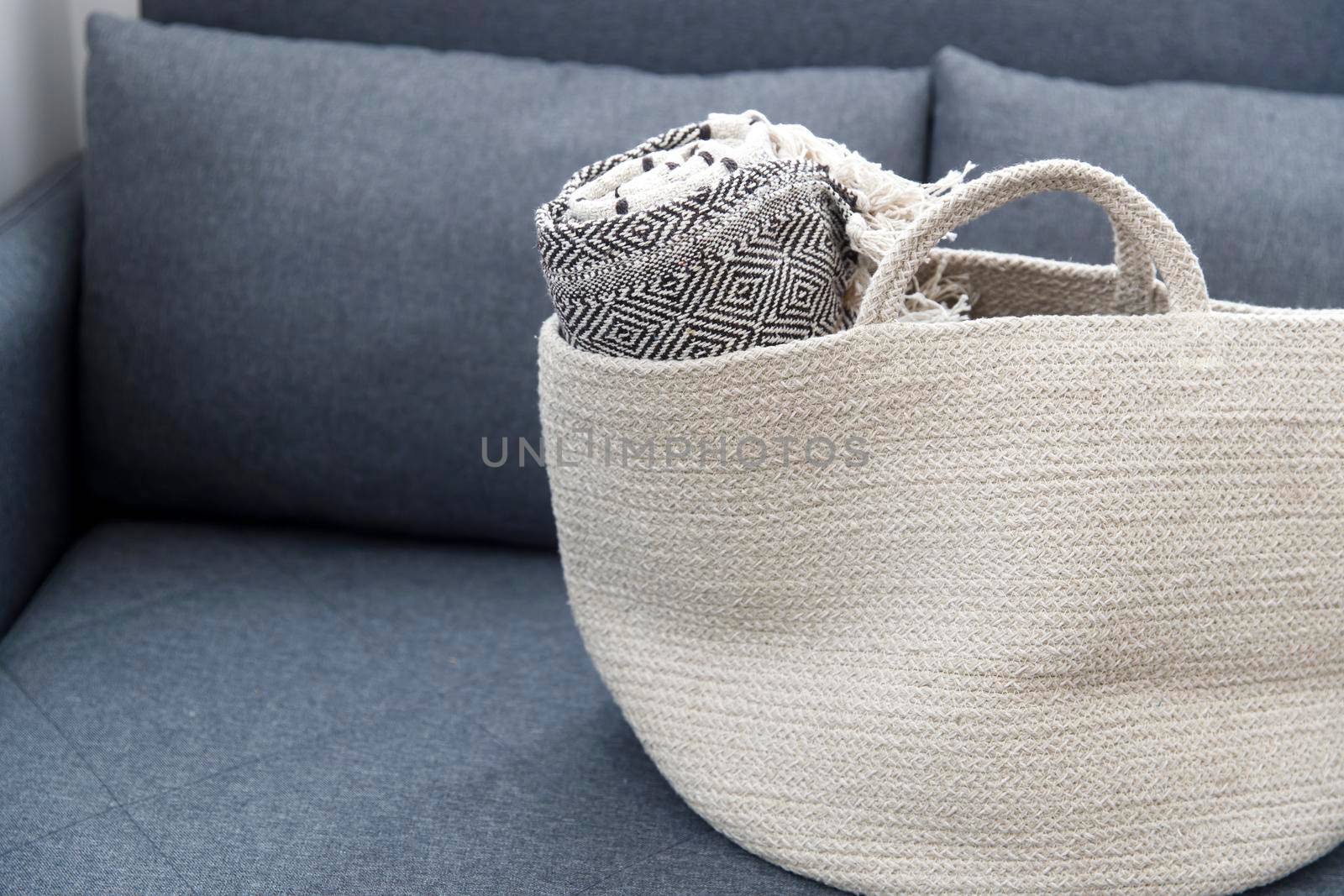 Tweed plaid rolled up in a wicker basket on a gray sofa by elenarostunova