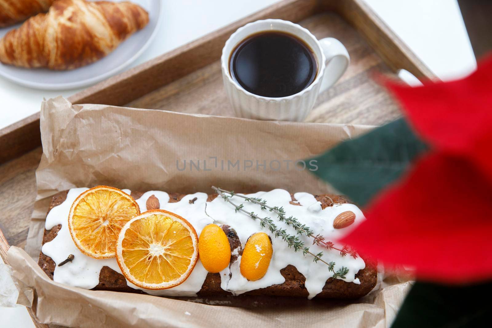 Freshly baked christmas cake and croissant on a gray round plate, a white cup of coffee and a garland on a tray on the table. Blooming poinsettia.