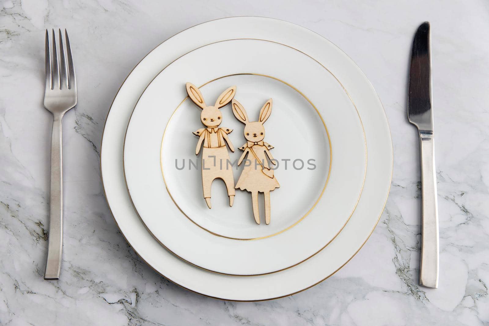 Serving spoon, fork, knife, and two carton bunny on the plate on the marble table. The concept of decoration for Easter.