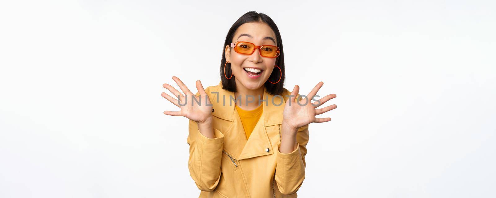 Surprised jazz hands. Happy asian girl smiling, looking amazed at camera, announcing smth, standing over white background.