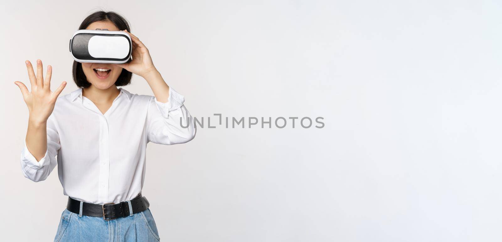 Vr chat. Asian girl saying hello in virtual reality glasses, smiling enthusiastic, concept of communication and future technology, white background by Benzoix