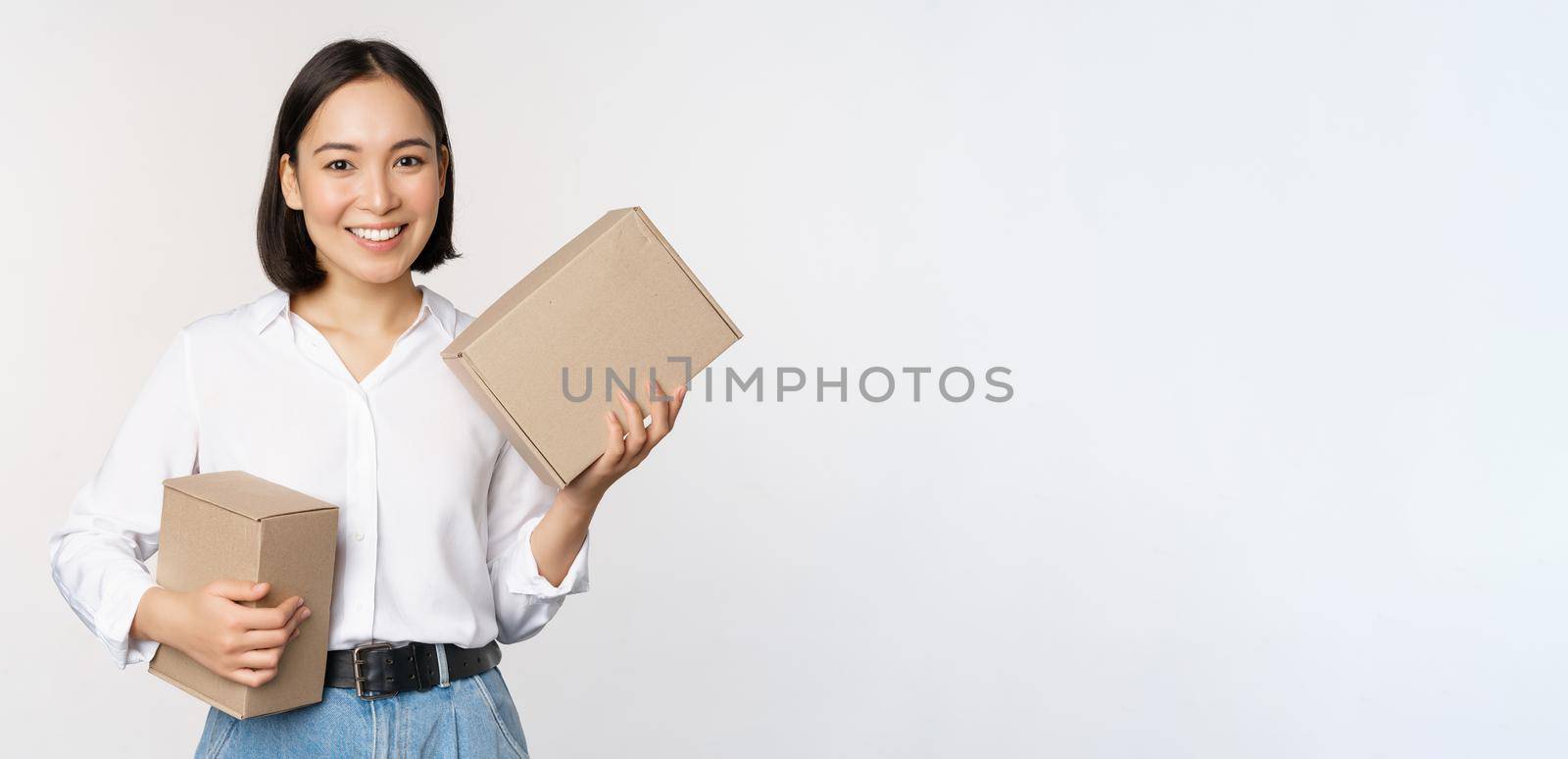 Concept of shopping and delivery. Young happy asian woman posing with boxes and smiling, standing over white background.