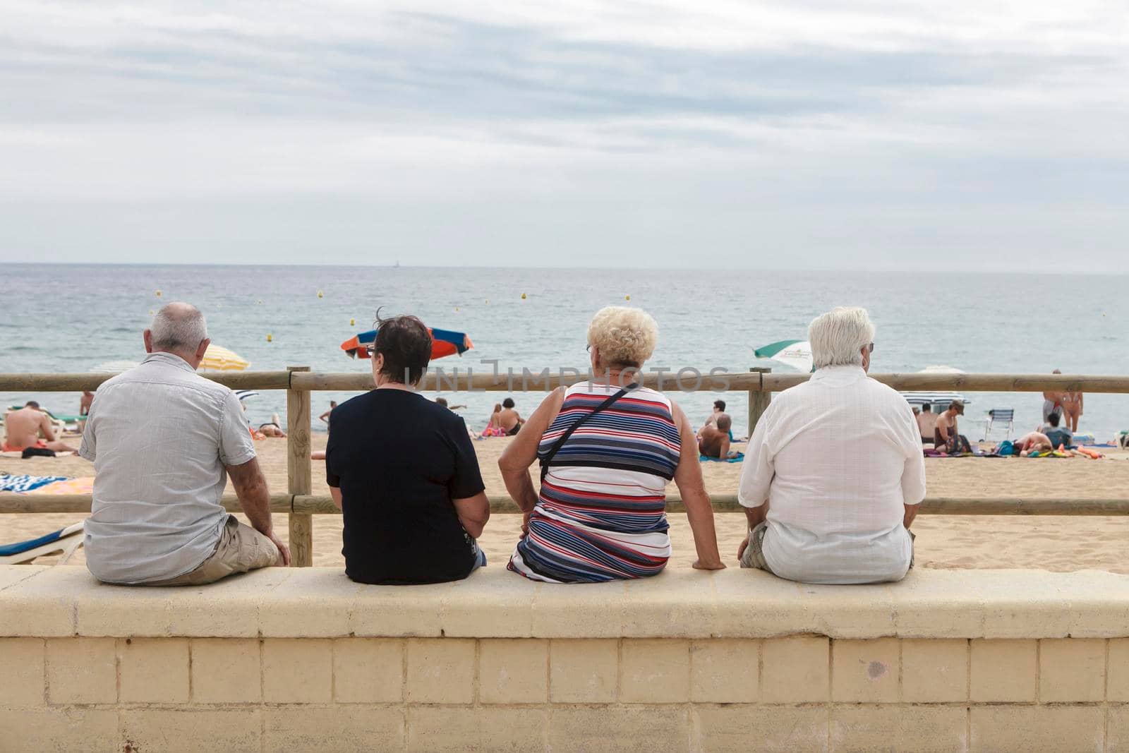 Blanes, Catalonia, Spain. - 25 July 2017, A company of elderly people are sitting on the parapet, looking at the sea. View from the back